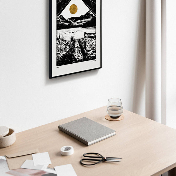 Desk with a notebook, scissors, and glass of water, framed picture on the wall.