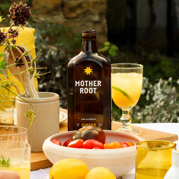 Mother Root non-alcoholic ginger drink bottle on a table with a glass of lemonade and fruit.