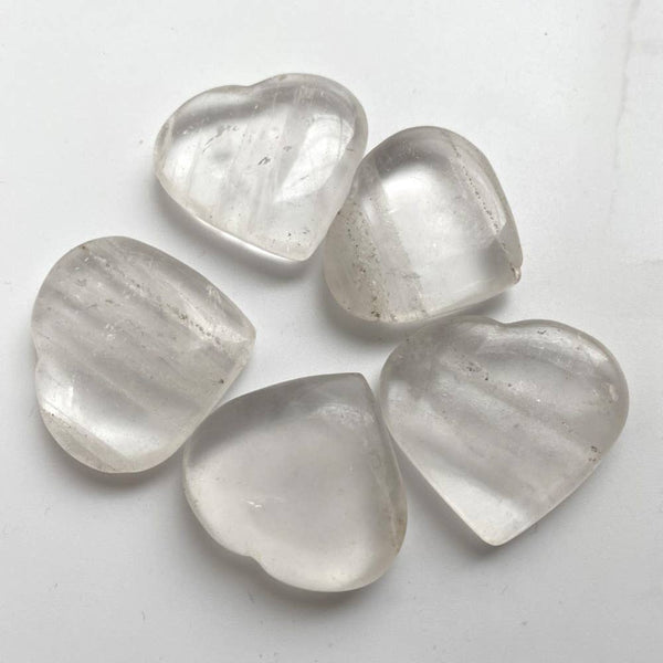 Five clear quartz heart-shaped crystals on a light grey background
