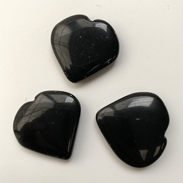 Three black obsidian heart-shaped crystals on a white background