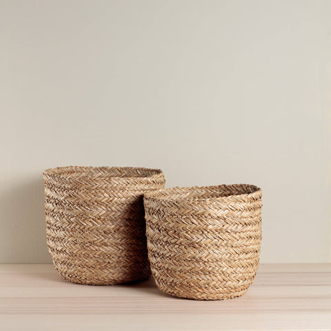 Two woven baskets on a wooden surface with a plain background