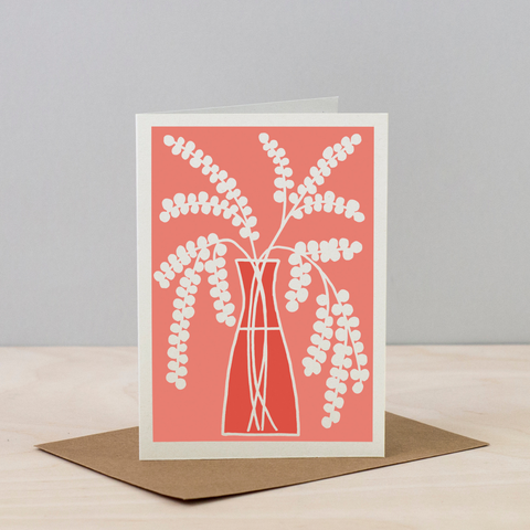 Greeting card with white floral design on a coral background, placed on a beige surface with a gray background.