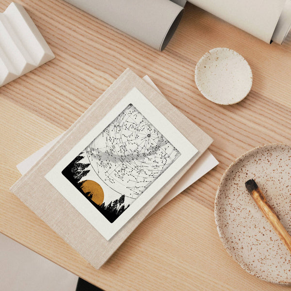 Star map greeting card on a wooden surface with ceramic bowls and a brush.