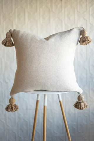Beige pillow with tassels on a white stand against a neutral background