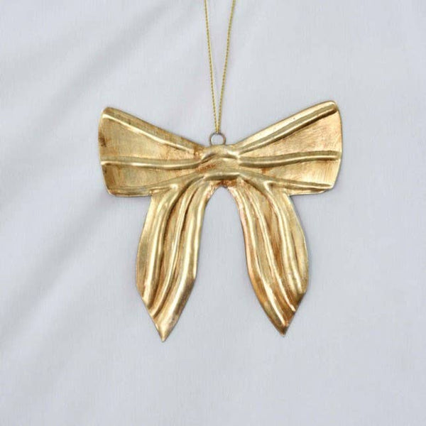 A gold bow-shaped decoration hanging from a thin gold thread against a light grey fabric background.