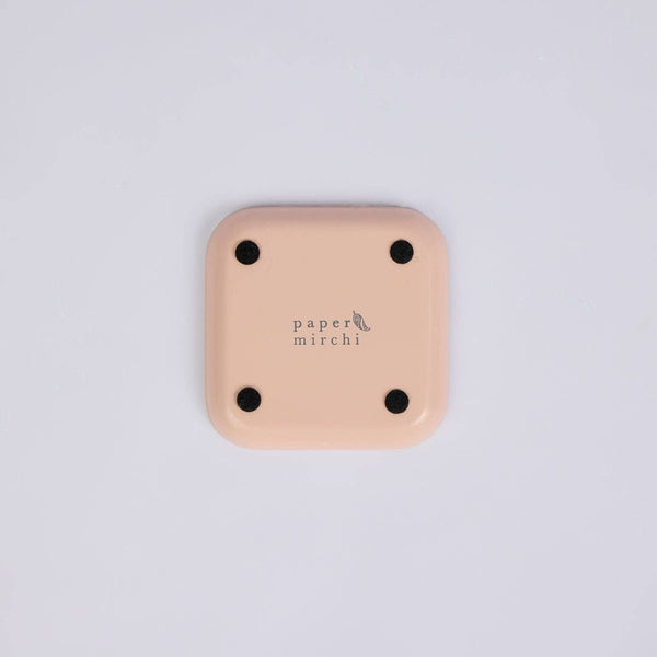 The back of a square, peach-coloured coaster with rounded corners and the 'paper mirchi' brand name printed in the centre, shown on a light grey background.