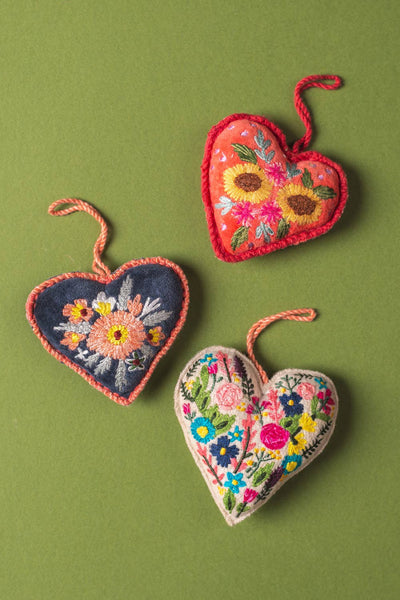 Three embroidered heart-shaped ornaments with floral patterns on a green background