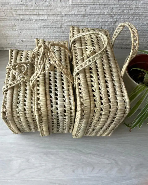 Three woven baskets with handles on a light wooden surface.