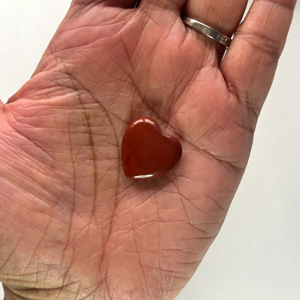 Heart-shaped red jasper gemstone held in a hand with a white background