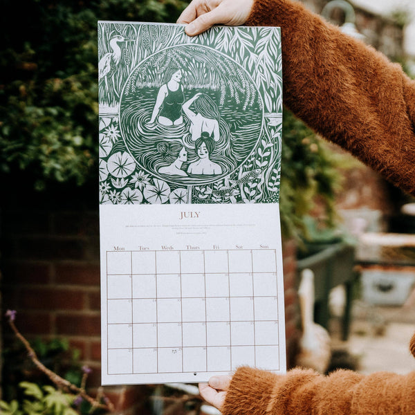 Person holding a calendar with a green and white design, featuring women and nature elements.