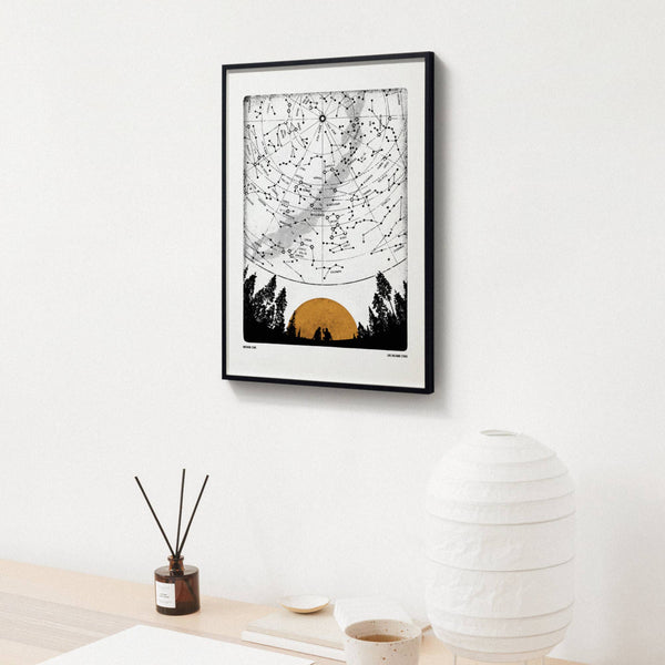 Framed artwork of a sunset over trees on a white wall with decor items below.