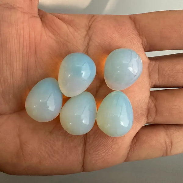 Five light blue opalite gemstones held in a hand against a neutral background