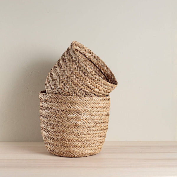 Two woven baskets on a wooden surface with a plain background