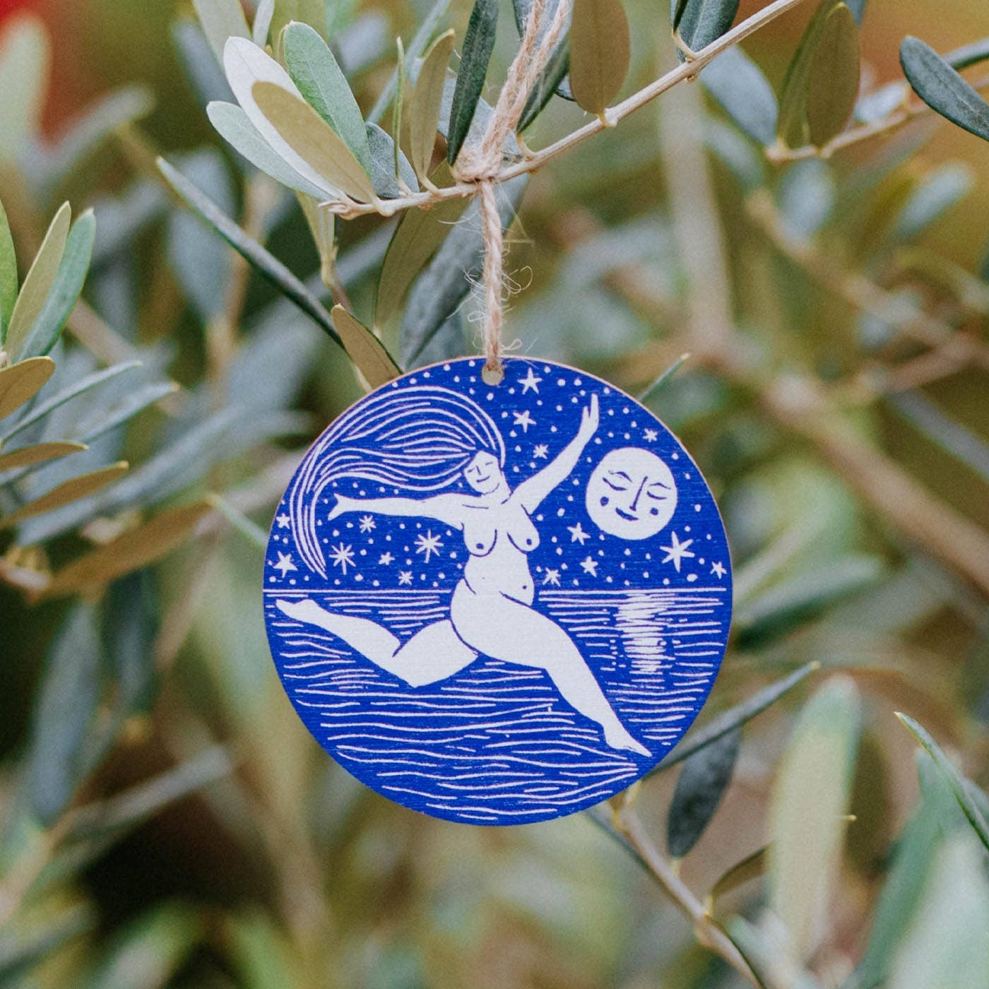 Blue decorative ornament with a woman and moon design hanging on a branch.