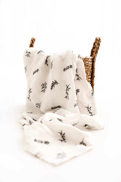 White blanket with black floral patterns draped over a wicker basket on a white background