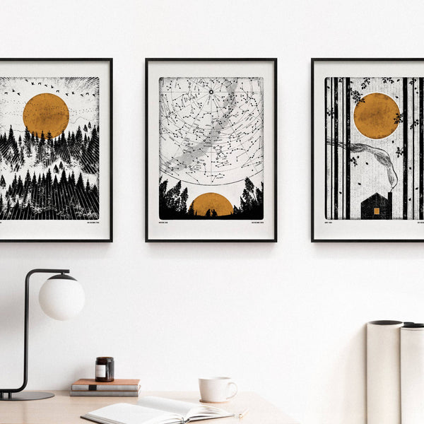 Three framed artworks with black and white designs and golden yellow accents on a wall.
