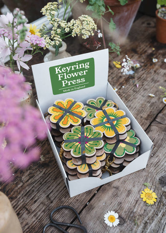 Keyring flower press in a box on a wooden surface with flowers around