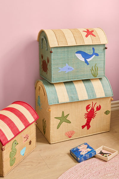 Stack of children's toy storage boxes with ocean-themed designs on a pink wall background.