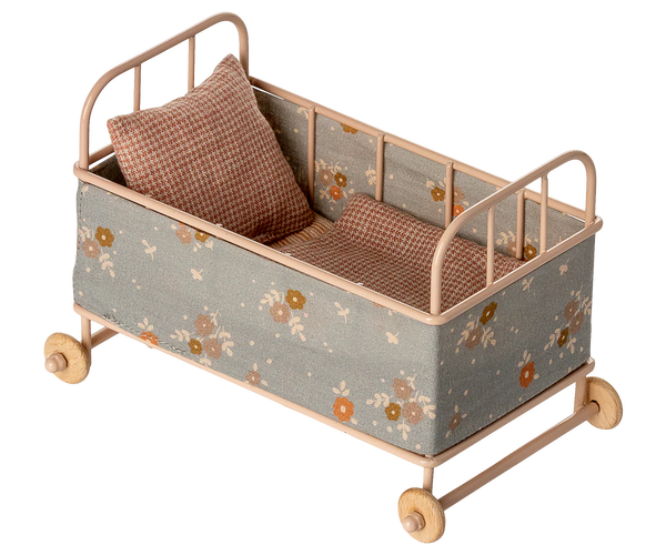 Small doll crib with floral pattern and wooden wheels on a white background