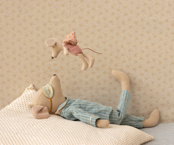 Stuffed toy mouse on a bed with a fairy mouse hanging above, with a patterned wall in the background