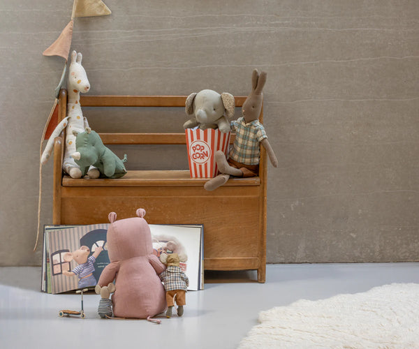Toy scene with stuffed animals on a wooden bench and a mirror, against a plain wall.