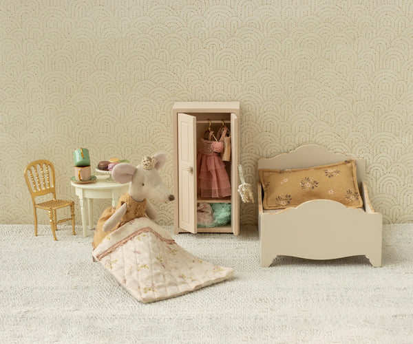 Miniature bedroom set with bed, chair, and wardrobe against a patterned wall.