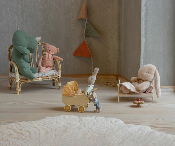 Miniature scene with stuffed animals on chairs and a baby carriage in a room.