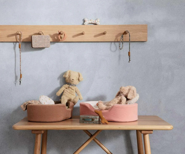 Wooden table with soft toy dogs and sleeping baskets against a grey wall.
