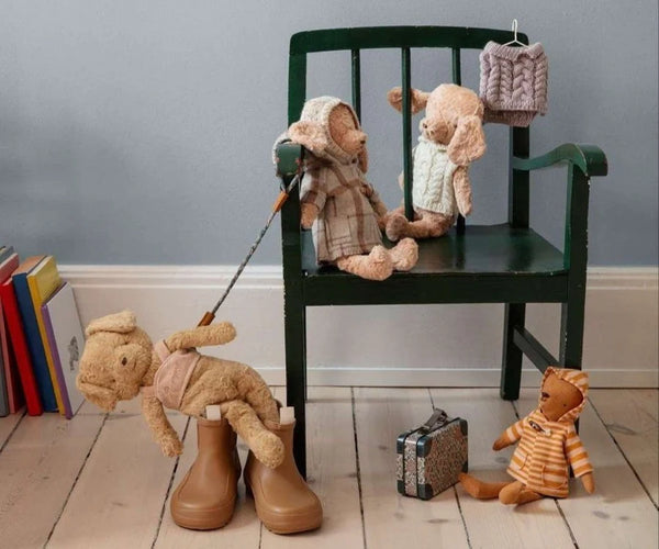 Stuffed animals on a chair with books and a suitcase on a wooden floor.