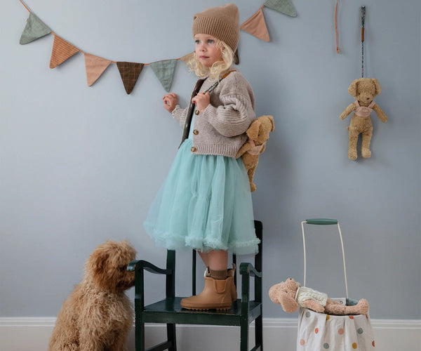 Child standing on a chair in a room with toys and a dog.