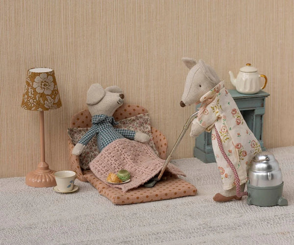 Two toy mice in a cozy room setting with a lamp, table, and chair.