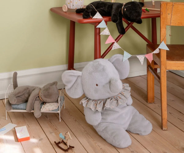 Children's room with a large grey elephant plush toy on the floor and a black cat on a red table.