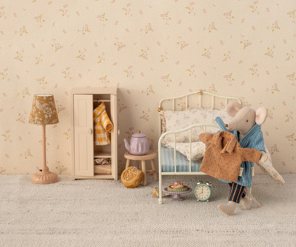 Children's bedroom with a bed, lamp, and toys against a floral wallpapered wall.