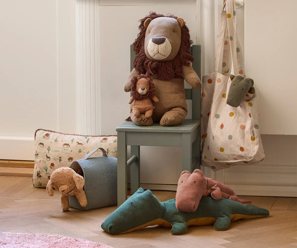 Plush toys including a lion, puppy and dinosaur on a chair and floor.