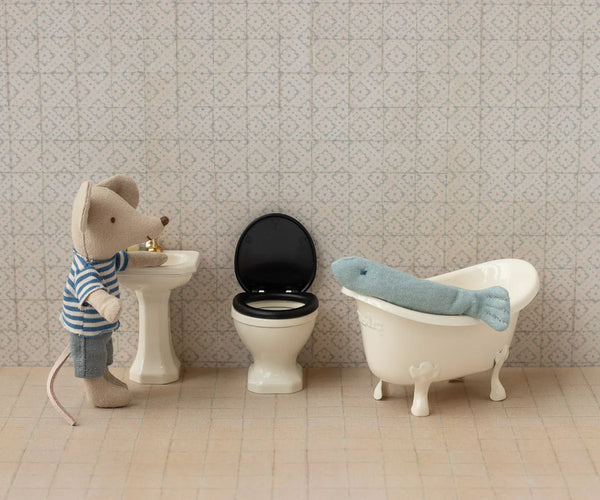 Miniature bathroom set with toy mouse, bathtub, toilet, and sink against a patterned wall.
