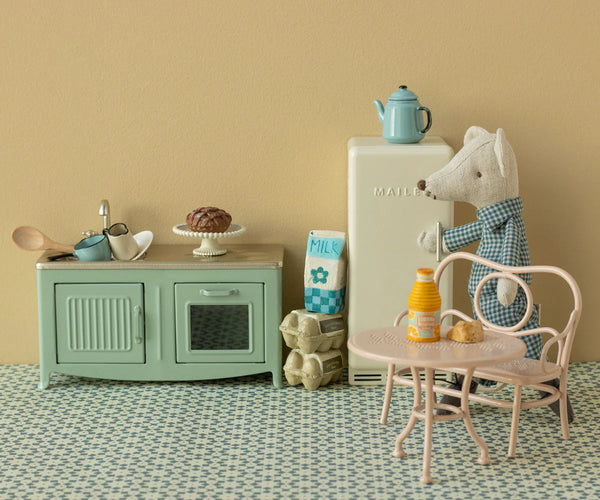 Miniature kitchen setup with a refrigerator, table, Kitchen sink, oven and toy mouse in checkered pyjamas.