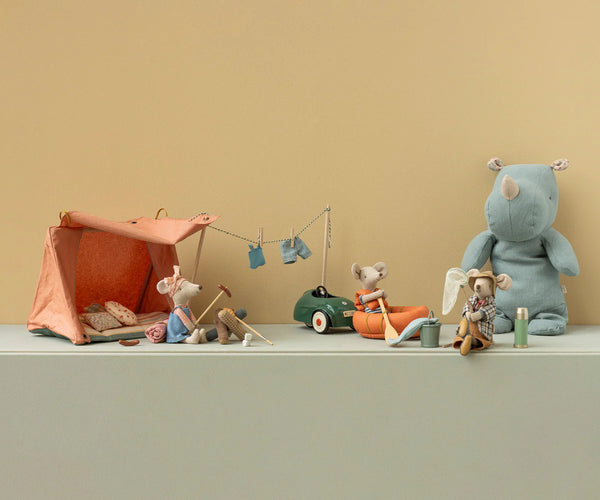 Set of toy animals with a tent and car on a light green surface against a beige wall.