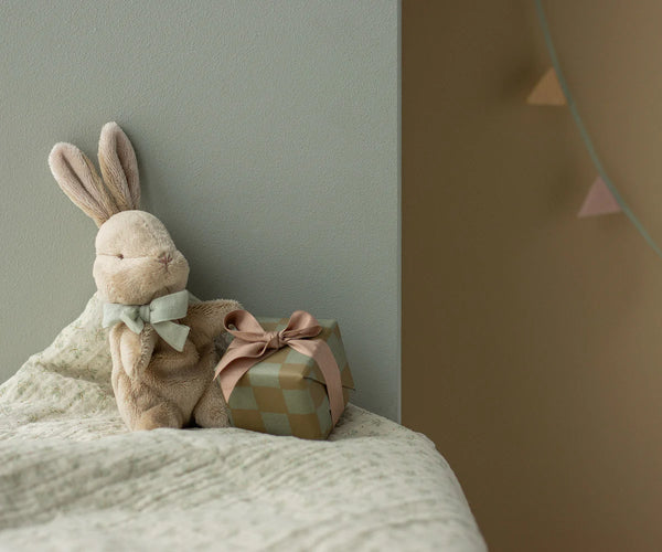Stuffed rabbit toy with a small gift box on a textured surface against a plain wall.