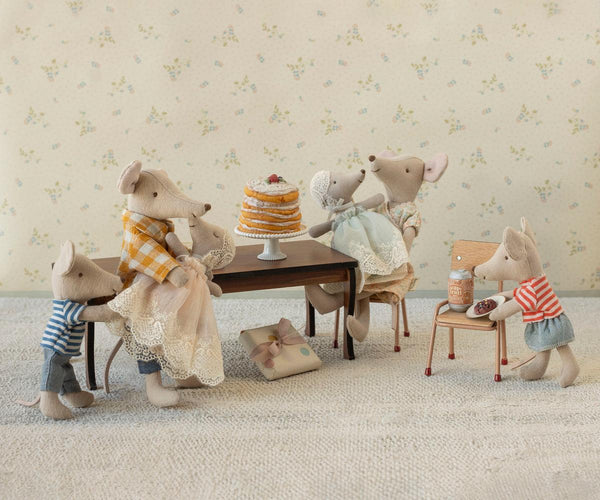 Miniature toy mice gathered around a table with a cake in a decorative setting.