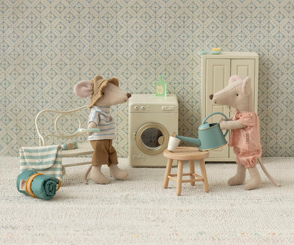 Two toy mice in a miniature room with a washing machine and other items.