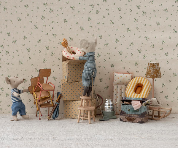 Miniature dollhouse scene with furniture and decorative items against a floral wallpaper background.