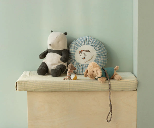Stuffed toy animals and a decorative cushion on a wooden surface against a light green wall.