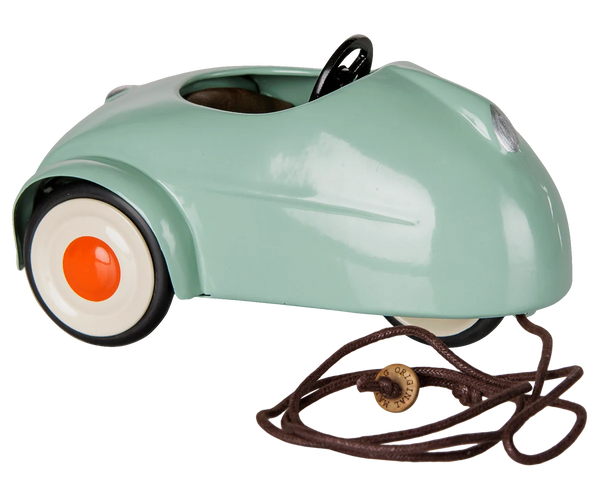 A retro-style miniature toy car in mint green with white wheels, orange centres, a black steering wheel, and a brown pull cord with a wooden knob, shown on a white background.
