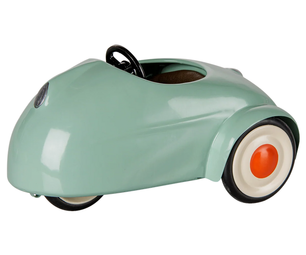 A retro-style miniature toy car in a glossy mint green finish, featuring a black steering wheel, black tires, and white-walled tires with orange center caps, shown on a plain white background.