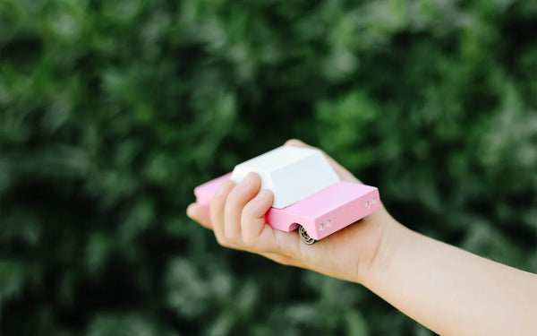 Pink toy car in a child's hand against an outdoor backdrop