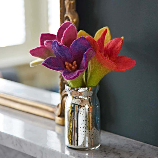 Colourful felt flowers in a silver vase on a marble surface with a mirror in the background.