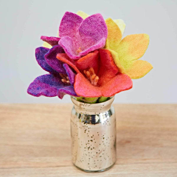 Colourful felt flowers in a small metallic vase on a wooden surface with a light grey background