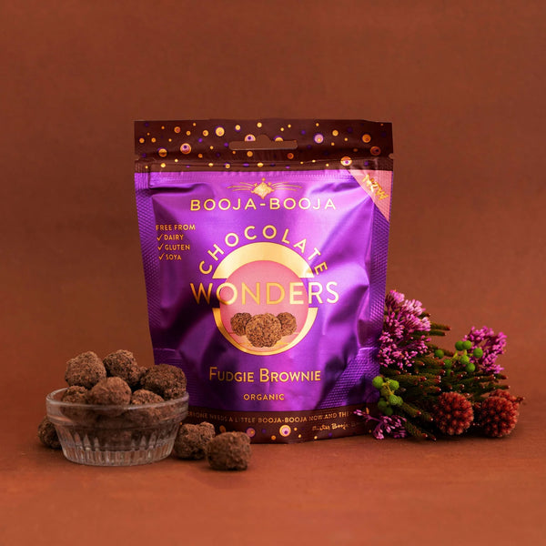 Booja-Booja Chocolate Wonders Fudgie Brownie packaging on a brown background with treats and flowers.