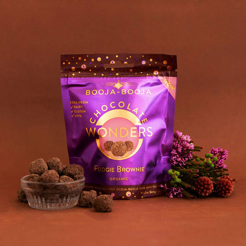 Booja-Booja Chocolate Wonders Fudgie Brownie packaging on a brown background with treats and flowers.