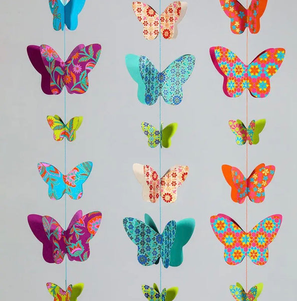 A set of colourful hanging butterfly decorations with floral patterns, suspended from thin strings against a plain light grey background.